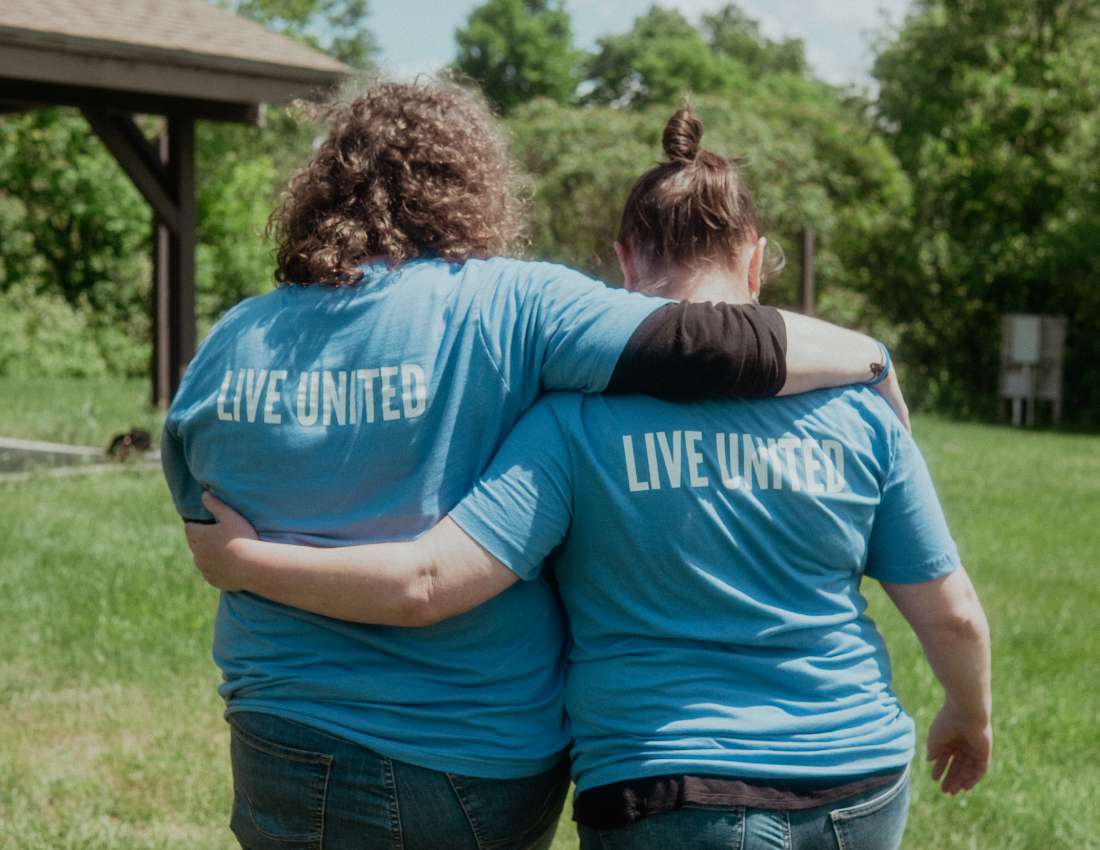 Two women walk with their arms on each other's shoulders wearing t-shirts that say Live United