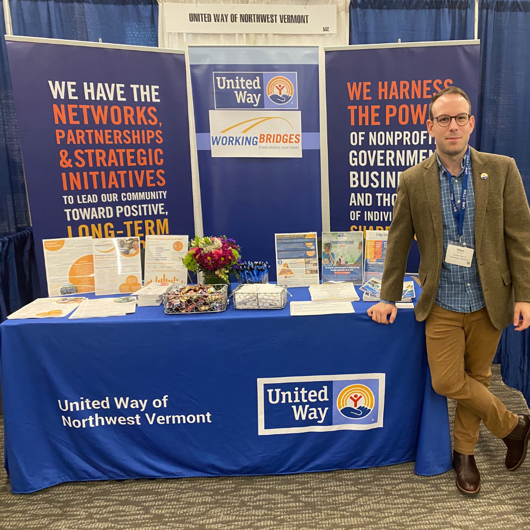 Dillon Boisvert stands in front of a United Way table display at the SHRM conference while wearing a brown blazer and a lanyard.