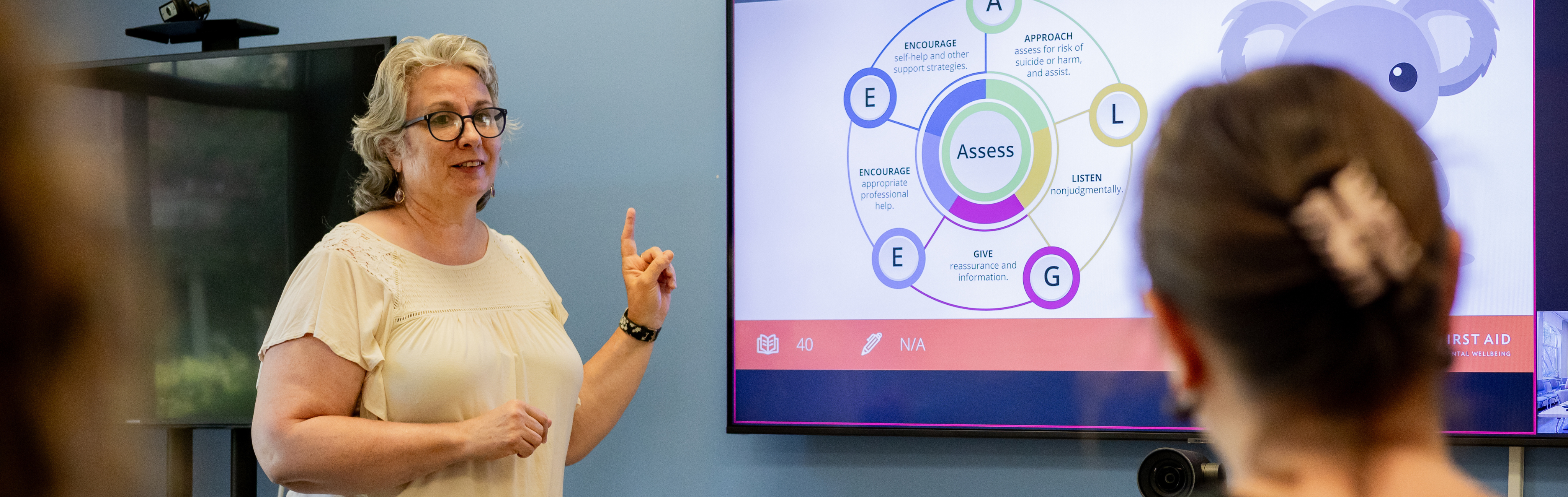 An image of Cari Kelley pointing to a screen during a Mental Health First Aid training