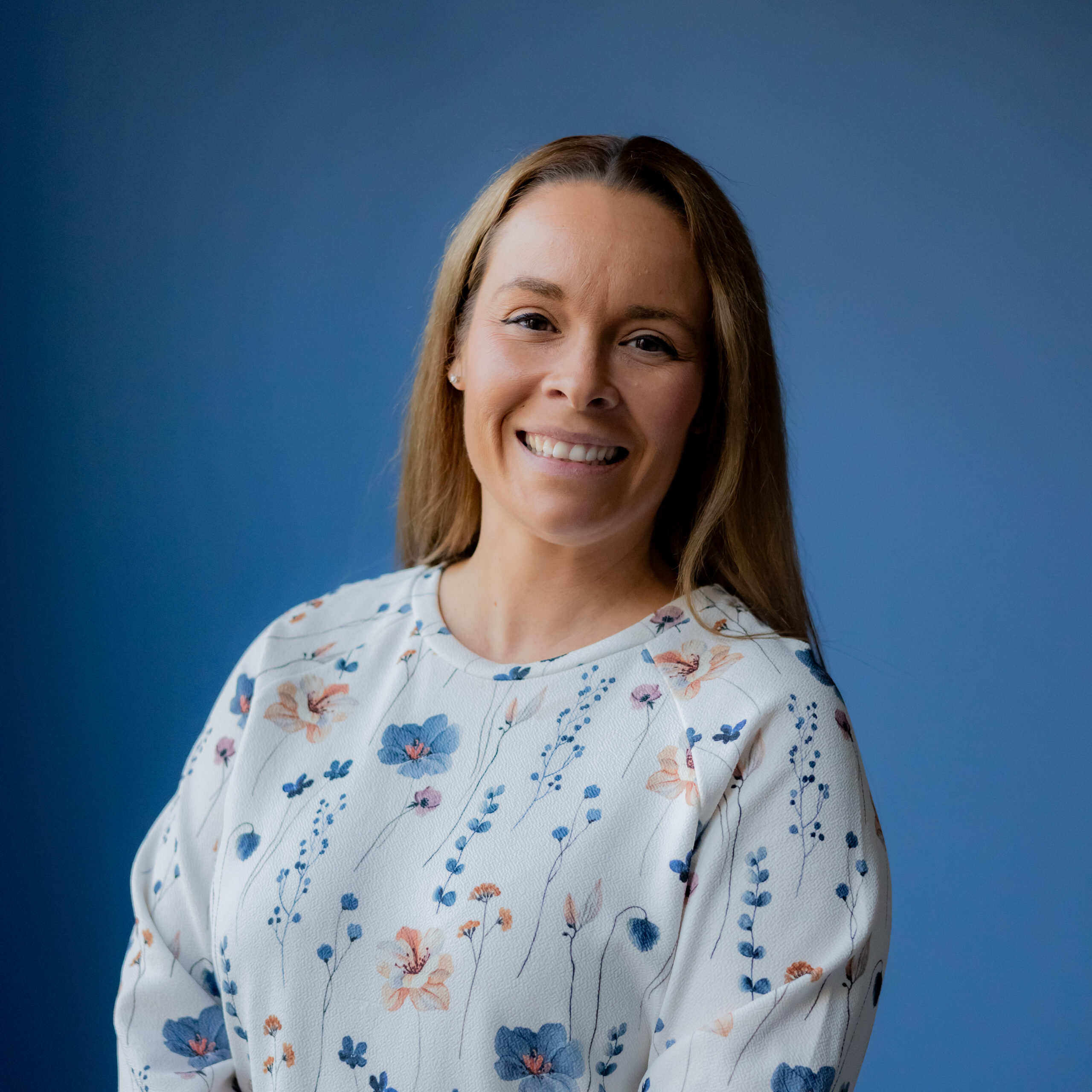 Ashley, wearing a white blouse with blue and orange floral print smiles at the camera.