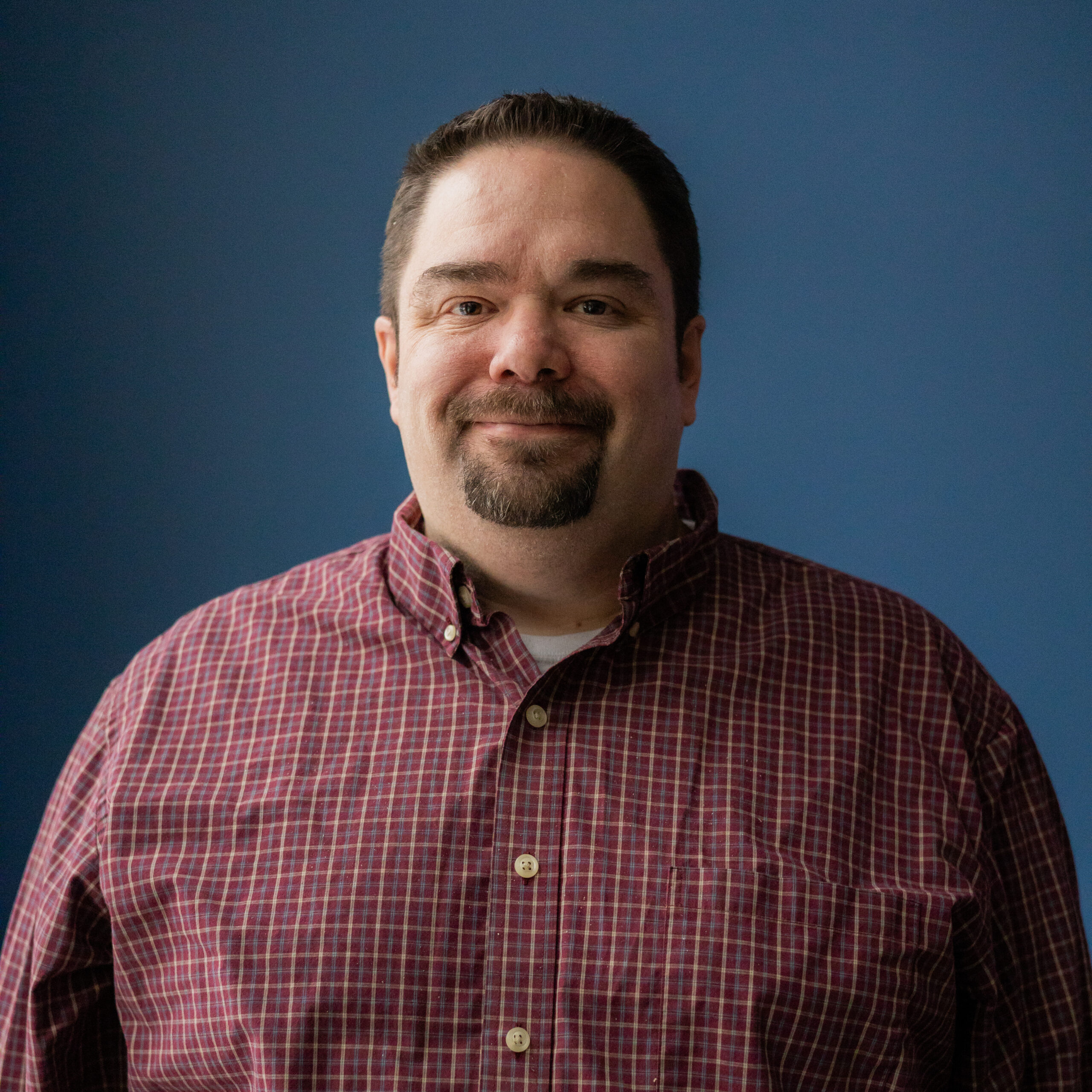 Jeff, wearing a red, collared shirt smiles at the camera.